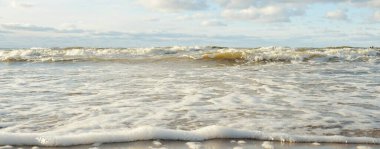 Kumlu bir sahilden (kum tepeleri) Baltık denizinin panoramik görüntüsü. Parlayan bulutlarla, dalgalarla ve su sıçramalarıyla berrak bir gökyüzü. Idyllic deniz manzarası. Sıcak kış havası, iklim değişikliği, doğa