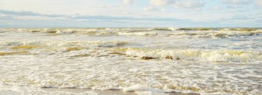 Kumlu bir sahilden (kum tepeleri) Baltık denizinin panoramik görüntüsü. Parlayan bulutlarla, dalgalarla ve su sıçramalarıyla berrak bir gökyüzü. Idyllic deniz manzarası. Sıcak kış havası, iklim değişikliği, doğa