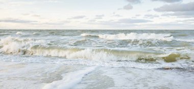 Gün batımında Baltık kıyıları (kum tepeleri). Yumuşak güneş ışığı, parlayan bulutlar, dalgalar ve su fışkıran berrak gökyüzü. Idyllic deniz manzarası. Liepaja, Letonya, Avrupa. Sıcak kış havası, iklim değişikliği, doğa
