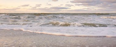Gün batımında Baltık kıyıları (kum tepeleri). Yumuşak güneş ışığı, parlayan bulutlar, dalgalar ve su fışkıran berrak gökyüzü. Idyllic deniz manzarası. Liepaja, Letonya, Avrupa. Sıcak kış havası, iklim değişikliği, doğa