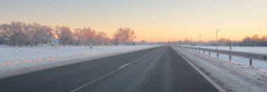 Karla kaplı orman ve kırsal alanda boş otoyol (asfalt yol). Gündoğumu, kar yağışı. Avrupa. Doğa, Noel tatilleri, uzak yerler, kış lastikleri, tehlikeli sürüş konsepti