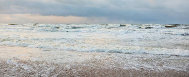 Fırtınadan sonra Baltık Denizi. Dramatik gökyüzü, parlayan bulutlar, yumuşak güneş ışığı. Dalgalar, su sıçratma. Resimli manzara, deniz manzarası, doğa. Panoramik görünüm
