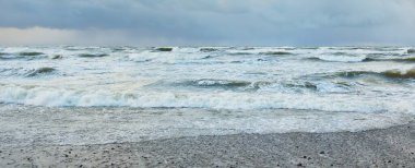Fırtınadan sonra Baltık Denizi. Dramatik gökyüzü, parlayan bulutlar, yumuşak güneş ışığı. Dalgalar, su sıçratma. Resimli manzara, deniz manzarası, doğa. Panoramik görünüm