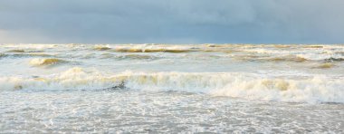 Fırtınadan sonra Baltık Denizi. Dramatik gökyüzü, parlayan bulutlar, yumuşak güneş ışığı. Dalgalar, su sıçratma. Resimli manzara, deniz manzarası, doğa. Panoramik görünüm