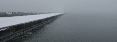 Kumlu sahilden Baltık Denizi 'nin panoramik manzarası. Deniz fenerine dolaş, dalgalar. Yoğun beyaz sis, sis, kar. Dalgalar, su sıçramaları. Deniz Burnu. Tek renkli kış manzarası