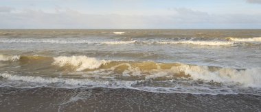 Kumlu bir sahilden (kum tepeleri) Baltık denizinin panoramik görüntüsü. Koyu bulutlu dramatik bir gökyüzü. Dalgalar, su sıçramaları. Idyllic deniz manzarası. Sıcak kış havası, iklim değişikliği, doğa. Danimarka