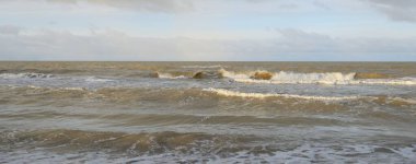 Kumlu bir sahilden (kum tepeleri) Baltık denizinin panoramik görüntüsü. Koyu bulutlu dramatik bir gökyüzü. Dalgalar, su sıçramaları. Idyllic deniz manzarası. Sıcak kış havası, iklim değişikliği, doğa. Danimarka