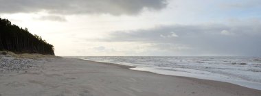Gün batımında Baltık kıyıları (kum tepeleri). Yumuşak güneş ışığı, parlayan bulutlar, dalgalar ve su fışkıran berrak gökyüzü. Idyllic deniz manzarası. Liepaja, Letonya, Avrupa. Sıcak kış havası, iklim değişikliği, doğa