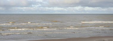 Kumlu bir sahilden (kum tepeleri) Baltık denizinin panoramik görüntüsü. Koyu bulutlu dramatik bir gökyüzü. Dalgalar, su sıçramaları. Idyllic deniz manzarası. Sıcak kış havası, iklim değişikliği, doğa. Danimarka