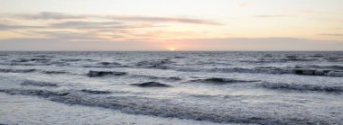 Gün batımında Baltık Denizi. Dramatik gökyüzü, mavi ve pembe parlayan bulutlar, altın güneş ışığı. Dalgalar, su sıçratma. Resimli manzara, deniz manzarası, doğa. Panoramik görünüm,