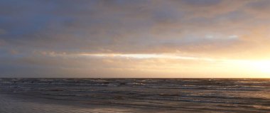 Fırtınadan sonra gün batımında Baltık Denizi. Dramatik gökyüzü, parlayan bulutlar, dofty altın güneş ışığı, dalgalar, fışkıran su. Resimli panoramik manzara. Doğa, çevre, ekoloji