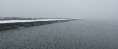 Kumlu sahilden Baltık Denizi 'nin panoramik manzarası. Deniz fenerine dolaş, dalgalar. Yoğun beyaz sis, sis, kar. Dalgalar, su sıçramaları. Deniz Burnu. Tek renkli kış manzarası