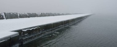 Kumlu sahilden Baltık Denizi 'nin panoramik manzarası. Deniz fenerine dolaş, dalgalar. Yoğun beyaz sis, sis, kar. Dalgalar, su sıçramaları. Deniz Burnu. Tek renkli kış manzarası