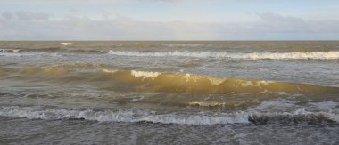 Kumlu bir sahilden (kum tepeleri) Baltık denizinin panoramik görüntüsü. Koyu bulutlu dramatik bir gökyüzü. Dalgalar, su sıçramaları. Idyllic deniz manzarası. Sıcak kış havası, iklim değişikliği, doğa. Danimarka