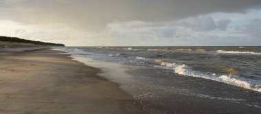 Gün batımında Baltık kıyıları (kum tepeleri). Yumuşak güneş ışığı, parlayan bulutlar, dalgalar ve su fışkıran berrak gökyüzü. Idyllic deniz manzarası. Liepaja, Letonya, Avrupa. Sıcak kış havası, iklim değişikliği, doğa