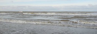 Kumlu bir sahilden (kum tepeleri) Baltık denizinin panoramik görüntüsü. Koyu bulutlu dramatik bir gökyüzü. Dalgalar, su sıçramaları. Idyllic deniz manzarası. Sıcak kış havası, iklim değişikliği, doğa. Danimarka