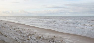 Kumlu bir sahilden (kum tepeleri) Baltık denizinin panoramik görüntüsü. Koyu bulutlu dramatik bir gökyüzü. Dalgalar, su sıçramaları. Idyllic deniz manzarası. Sıcak kış havası, iklim değişikliği, doğa. Danimarka
