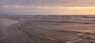 Fırtınadan sonra gün batımında Baltık Denizi. Dramatik gökyüzü, parlayan bulutlar, dofty altın güneş ışığı, dalgalar, fışkıran su. Resimli panoramik manzara. Doğa, çevre, ekoloji