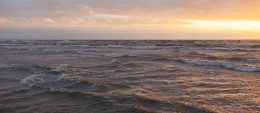 Fırtınadan sonra gün batımında Baltık Denizi. Dramatik gökyüzü, parlayan bulutlar, dofty altın güneş ışığı, dalgalar, fışkıran su. Resimli panoramik manzara. Doğa, çevre, ekoloji