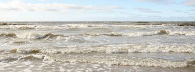 Fırtınadan sonra Baltık Denizi. Dramatik gökyüzü, parlayan bulutlar, yumuşak güneş ışığı. Dalgalar, su sıçratma. Resimli manzara, deniz manzarası, doğa. Panoramik görünüm
