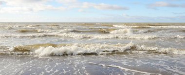 Fırtınadan sonra Baltık Denizi. Dramatik gökyüzü, parlayan bulutlar, yumuşak güneş ışığı. Dalgalar, su sıçratma. Resimli manzara, deniz manzarası, doğa. Panoramik görünüm