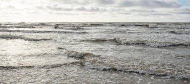 Fırtınadan sonra Baltık Denizi. Dramatik gökyüzü, parlayan bulutlar, yumuşak güneş ışığı. Dalgalar, su sıçratma. Resimli manzara, deniz manzarası, doğa. Panoramik görünüm