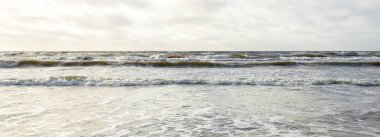 Kumlu sahilden Baltık denizinin panoramik görüntüsü (kum tepeleri). Parlak bulutlu dramatik bir gökyüzü. Dalgalar, su sıçramaları. Idyllic deniz manzarası. Bahar havası, iklim değişikliği, doğa