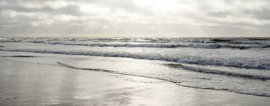 Kumlu sahilden Baltık denizinin panoramik görüntüsü (kum tepeleri). Parlak bulutlu dramatik bir gökyüzü. Dalgalar, su sıçramaları. Idyllic deniz manzarası. Bahar havası, iklim değişikliği, doğa