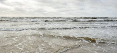 Kumlu sahilden Baltık denizinin panoramik görüntüsü (kum tepeleri). Parlak bulutlu dramatik bir gökyüzü. Dalgalar, su sıçramaları. Idyllic deniz manzarası. Bahar havası, iklim değişikliği, doğa