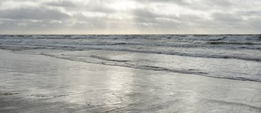 Kumlu sahilden Baltık denizinin panoramik görüntüsü (kum tepeleri). Parlak bulutlu dramatik bir gökyüzü. Dalgalar, su sıçramaları. Idyllic deniz manzarası. Bahar havası, iklim değişikliği, doğa