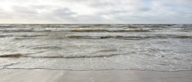 Kumlu sahilden Baltık denizinin panoramik görüntüsü (kum tepeleri). Parlak bulutlu dramatik bir gökyüzü. Dalgalar, su sıçramaları. Idyllic deniz manzarası. Bahar havası, iklim değişikliği, doğa
