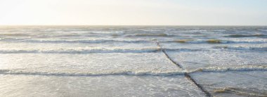 Gün batımında Baltık kıyısı. Yumuşak altın güneş ışığı, parlayan gökyüzü, dalgalar. Idyllic deniz manzarası. Seyahat yerleri, eko turizm, doğa, hava durumu, iklim değişikliği. Resimli panoramik manzara