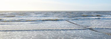 Gün batımında Baltık kıyısı. Yumuşak altın güneş ışığı, parlayan gökyüzü, dalgalar. Idyllic deniz manzarası. Seyahat yerleri, eko turizm, doğa, hava durumu, iklim değişikliği. Resimli panoramik manzara
