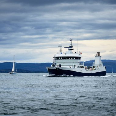 Bulutlu bir günde, iç Hebrides adalarındaki kayalıkların, dağların ve vadilerin panoramik manzarası. İskoçya, İngiltere. Beyaz yelkenli tekne ve balıkçı teknesi.