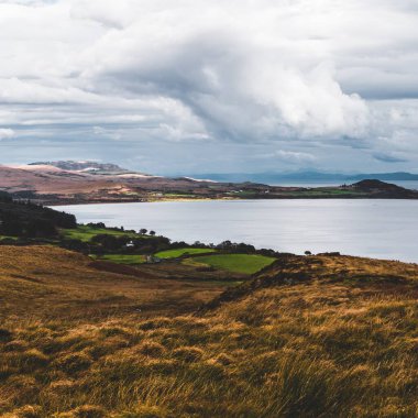 Jura adasının kıyıları, dağları ve vadilerinin panoramik hava manzarası. Bulutlu mavi gökyüzü. Fırtınalı hava. Paps of Jura, Inner Hebrides, İskoçya, İngiltere. Seyahat yerleri, turizm, ulusal simgeler