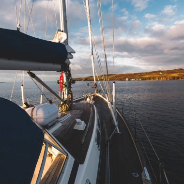 Günbatımında Islay Adası kıyısında seyir halindeki ahşap meşe güvertesiyle donatılmış modern bir yat. Inner Hebrides, İskoçya, İngiltere. Spor ve eğlence, seyahat yerleri, dönüm noktaları, ulaşım