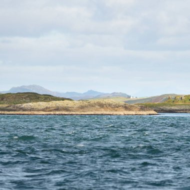 Jura adasının kıyılarının panoramik manzarası, dağları ve vadileri sudan. Bulutlu mavi gökyüzü. Paps of Jura, Inner Hebrides, İskoçya, İngiltere