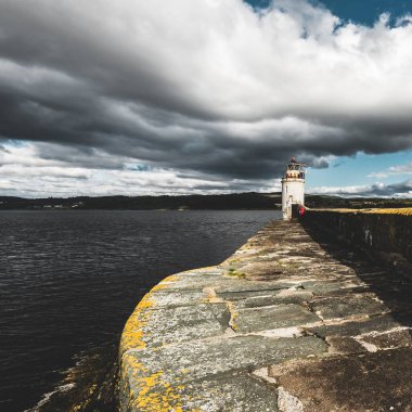 Eski deniz fenerine doğru boş bir gezinti, yakın plan. Arka planda kayalık kıyılar var. Dramatik bulut manzarası. Ardrishaig, Crinan Kanalı, İskoçya, İngiltere. Seyahat yerleri, gezi teması