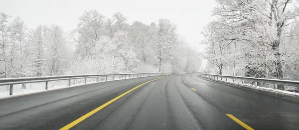 Karla kaplı ormanda boş otoyol (asfalt yol). Kanada mı? Doğa, Noel tatilleri, uzak yerler, kış lastikleri, tehlikeli sürüş konsepti