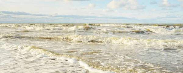 Kumlu bir sahilden (kum tepeleri) Baltık denizinin panoramik görüntüsü. Parlayan bulutlarla, dalgalarla ve su sıçramalarıyla berrak bir gökyüzü. Idyllic deniz manzarası. Sıcak kış havası, iklim değişikliği, doğa
