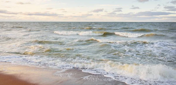 Gün batımında Baltık kıyıları (kum tepeleri). Yumuşak güneş ışığı, parlayan bulutlar, dalgalar ve su fışkıran berrak gökyüzü. Idyllic deniz manzarası. Liepaja, Letonya, Avrupa. Sıcak kış havası, iklim değişikliği, doğa