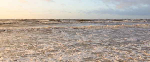 Baltic sea at sunset. Dramatic sky, blue and pink glowing clouds, golden sunlight. Waves, splashing water. Picturesque scenery, seascape, nature. Panoramic view,