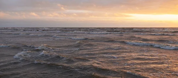 Fırtınadan sonra gün batımında Baltık Denizi. Dramatik gökyüzü, parlayan bulutlar, dofty altın güneş ışığı, dalgalar, fışkıran su. Resimli panoramik manzara. Doğa, çevre, ekoloji