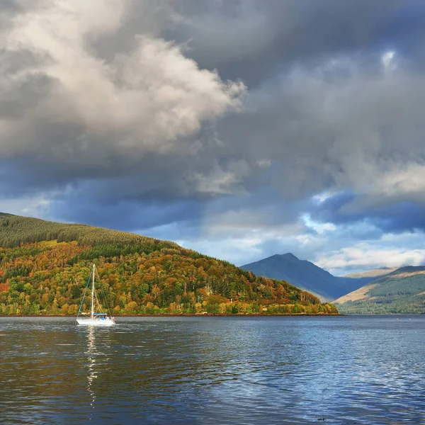 Loch Fyne yakınlarındaki sahil, orman ve tepelerin manzarası. Beyaz yelkenli yatla yakın plan. Inveraray, Inner Hebrides, Argyll ve Bute, İskoçya, İngiltere