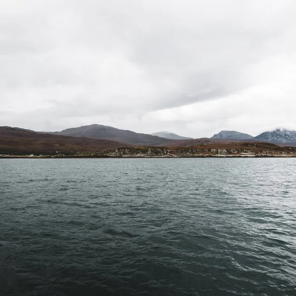 Panoramic view of the rocky shore near the mountain peaks of Paps of Jura under the cloudy blue sky. A view from the yacht. Jura island, Inner Hebrides, Scotland, UK. Travel destinations, landmarks