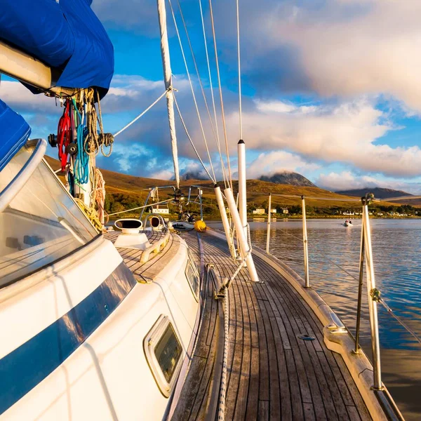 Sloop rigged modern yacht with wooden teak deck sailing near the rocky shore of Jura island at sunset, close-up. Inner Hebrides, Scotland, UK. Sport, recreation, cruise, travel destinations