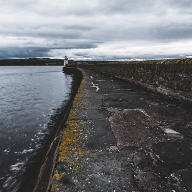 Eski deniz fenerine doğru boş bir gezinti, yakın plan. Arka planda kayalık kıyılar var. Dramatik bulut manzarası. Ardrishaig, Crinan Kanalı, İskoçya, İngiltere. Seyahat yerleri, gezi teması