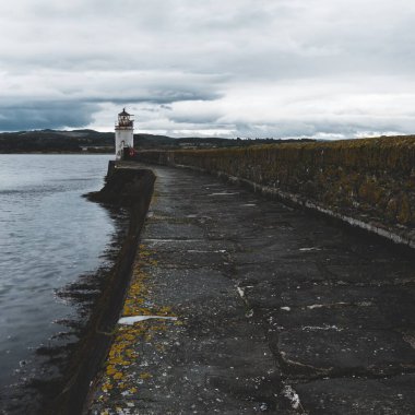 Eski deniz fenerine doğru boş bir gezinti, yakın plan. Arka planda kayalık kıyılar var. Dramatik bulut manzarası. Ardrishaig, Crinan Kanalı, İskoçya, İngiltere. Seyahat yerleri, gezi teması
