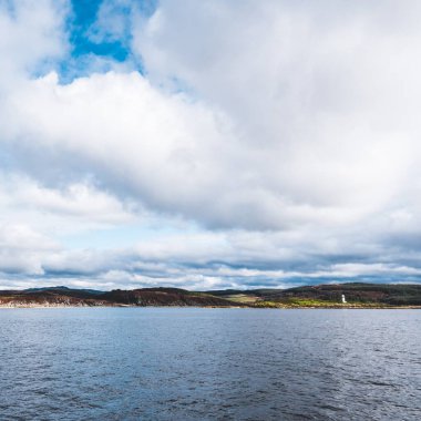 Dramatik gökyüzü altında Tarbert 'in kayalık kıyılarının panoramik manzarası. Arka planda deniz feneri, İskoçya, İngiltere. Seyahat yerleri, ulusal dönüm noktası, eğlence, eko turizm, tatiller
