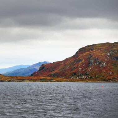 Bute 'un kayalık kıyılarının sudan panoramik görüntüsü. Tepeler ve dağlar arka planda. Karanlık fırtına gökyüzü. Bute Adası, Clyde Firth, İskoçya, İngiltere